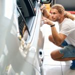 Odborník opravuje preliačinu na karosérii automobilu po poškodení vandalizmom.