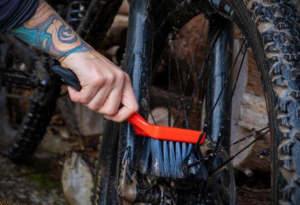 Údržba bicykla pomocou červenej servisnej kefy na odstránenie nečistôt z pohyblivých častí.